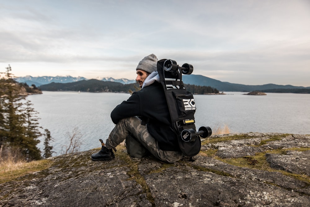 a man sitting on top of a rock next to a body of water