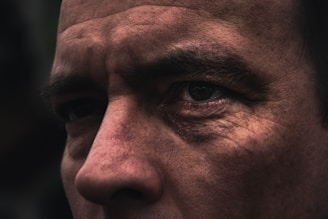 A close-up of a person's face highlighting the texture of the skin and wrinkles around the eyes. The lighting emphasizes the contours and details of the facial features.