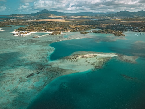 A vibrant aerial view of Mauritius coastline with turquoise waters and lush greenery under a bright sky.