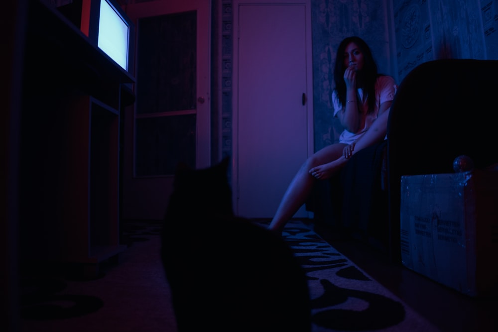 a woman sitting on a bed in a dark room next to a black cat