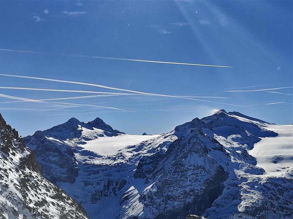 a view of a snowy mountain range with contrails in the sky