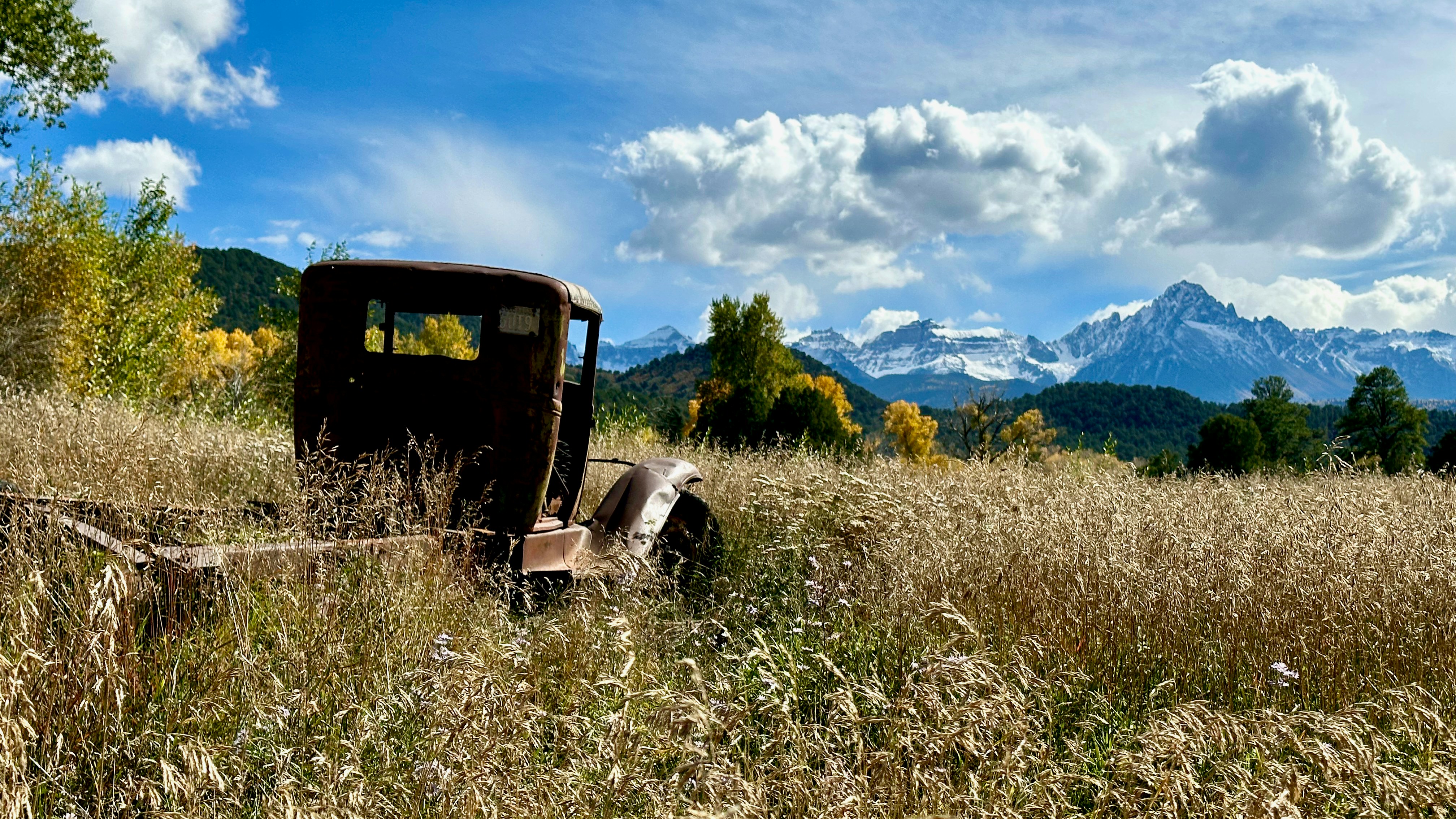 an old truck in a field with mountains in the background