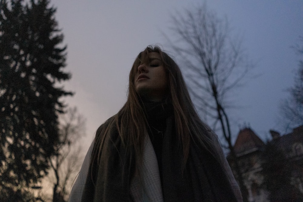 a woman with long hair standing in front of a tree