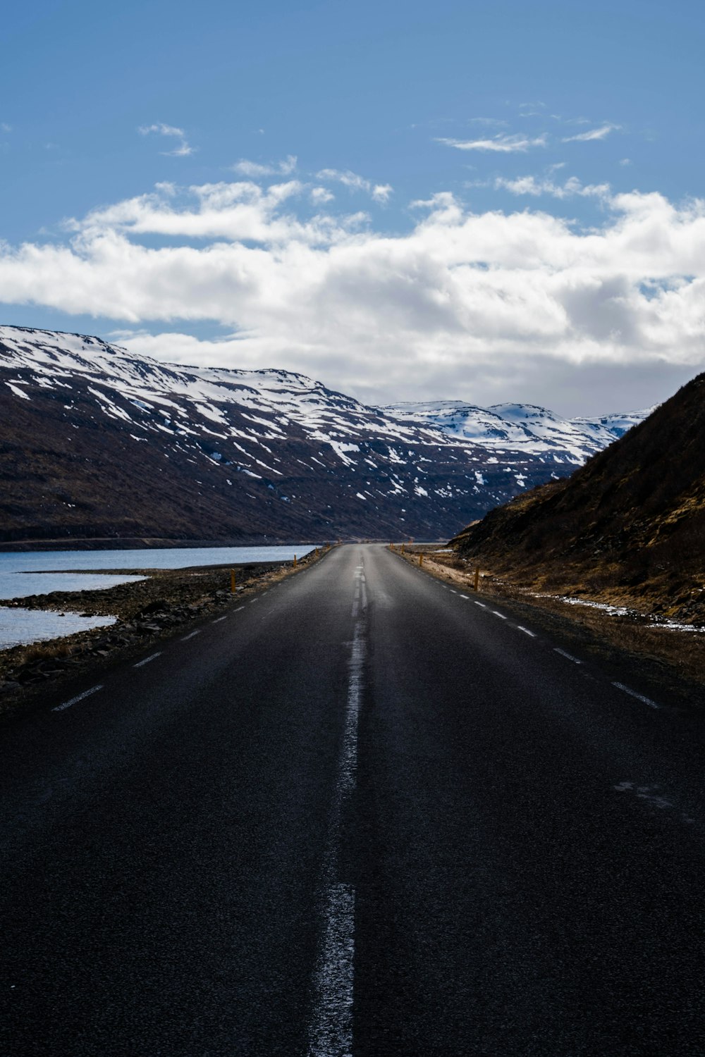 an empty road with snow covered mountains in the background