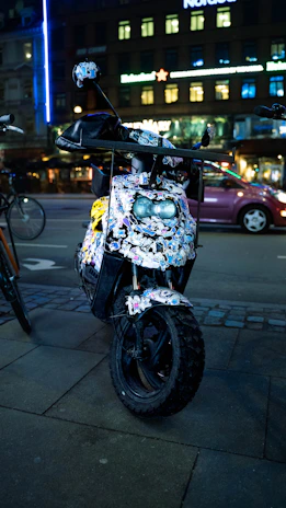A compact scooter parked beside a city sidewalk with vibrant street art in the background.