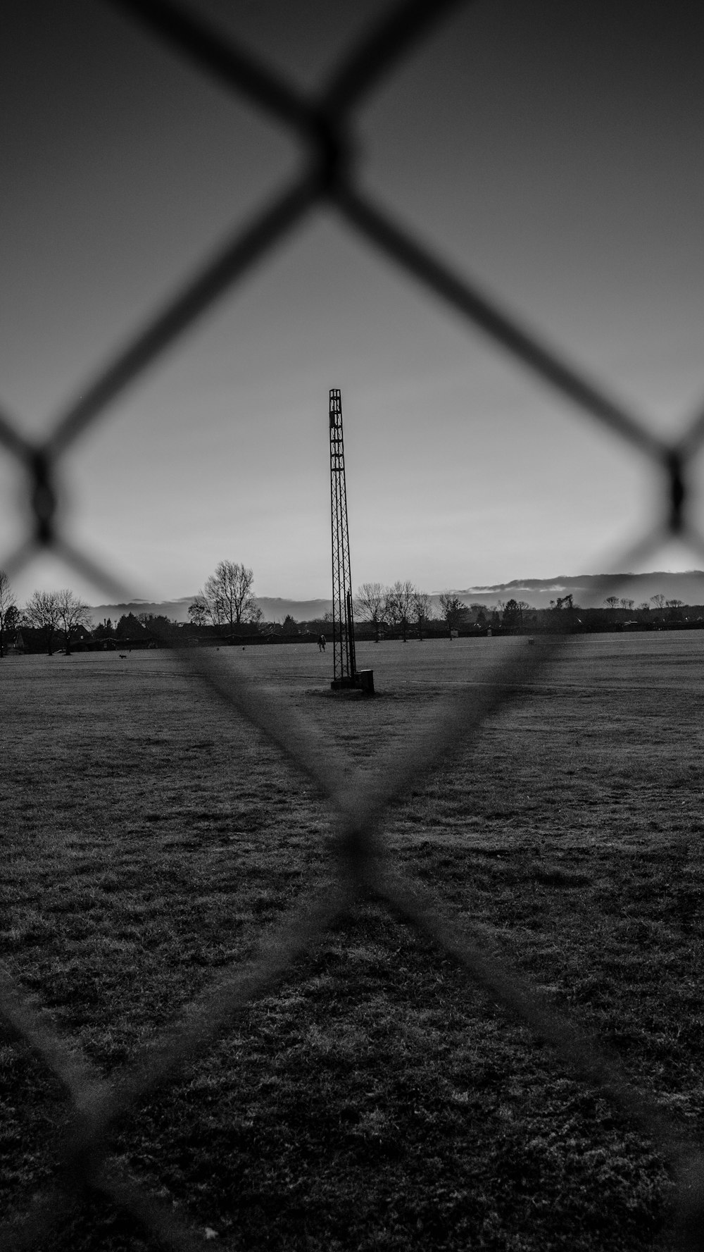 a black and white photo of a field behind a fence