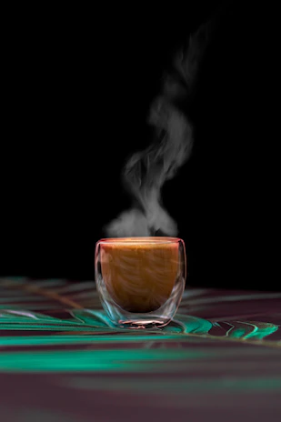 Elegant dark-themed photo of a steaming cup of coffee on a black surface with warm cream and subtle gold accents in the background.
