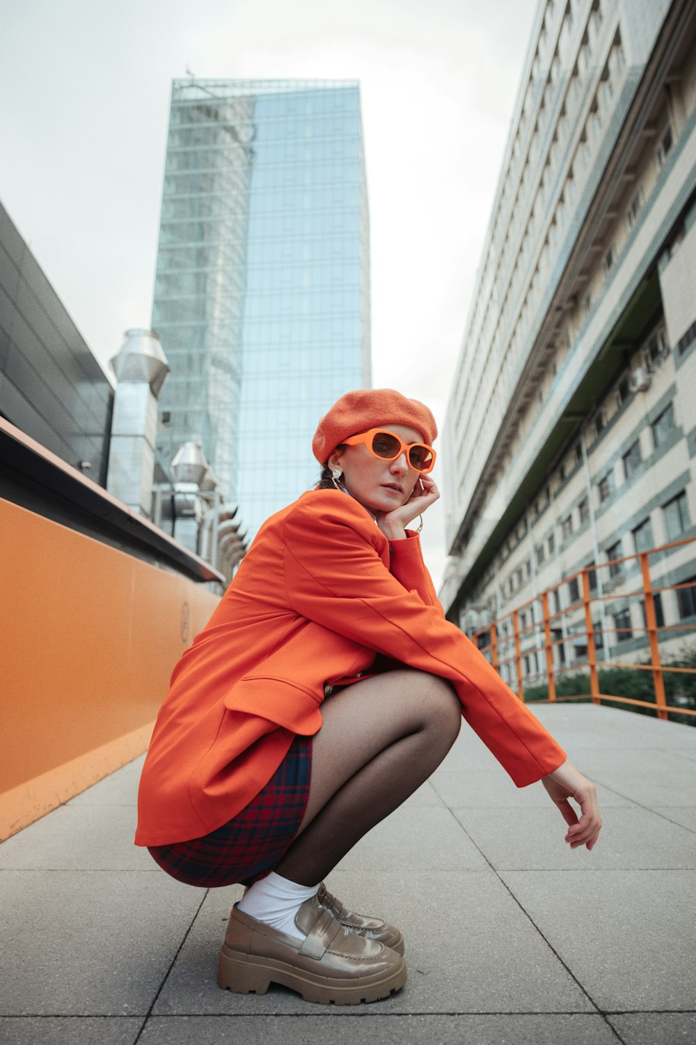 a woman in an orange coat and hat squatting on a sidewalk