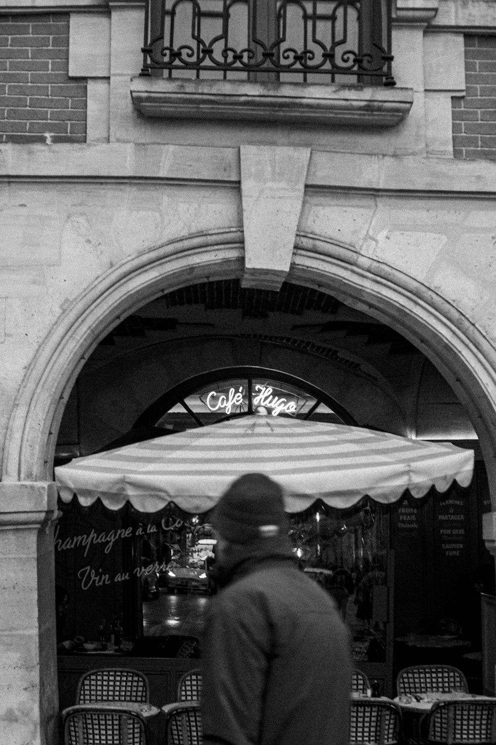a black and white photo of a man standing in front of a restaurant