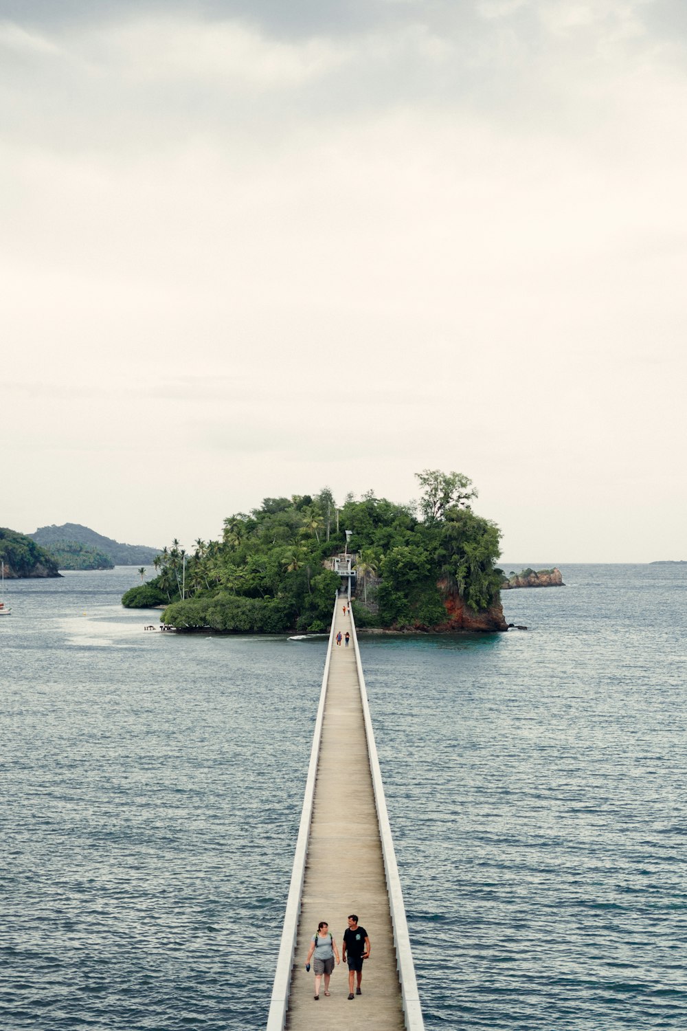 two people walking down a pier towards a small island