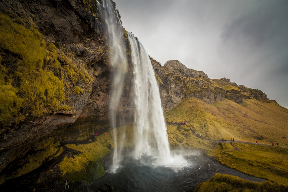 a large waterfall with people standing on the side of it