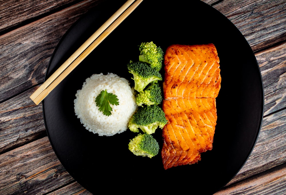 a black plate topped with salmon and broccoli