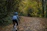 A cyclist riding a gravel bike on a sunlit forest trail with autumn leaves.