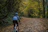 A cyclist riding a gravel bike on a sunlit forest trail with autumn leaves.