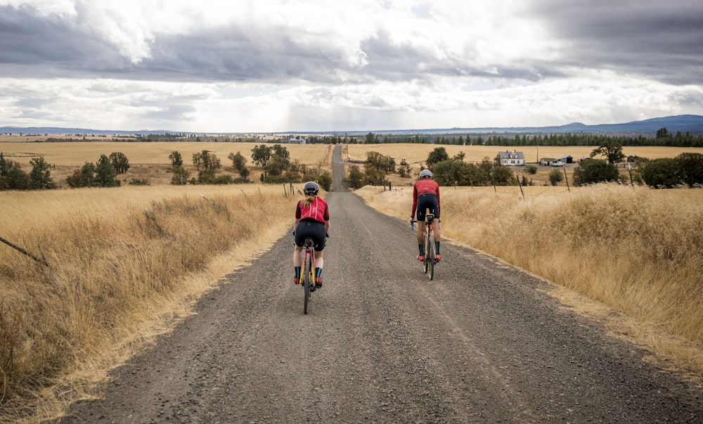 a couple of people riding bikes down a dirt road