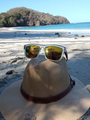 A stylish sunhat and polarized sunglasses resting on a deck chair overlooking the ocean.