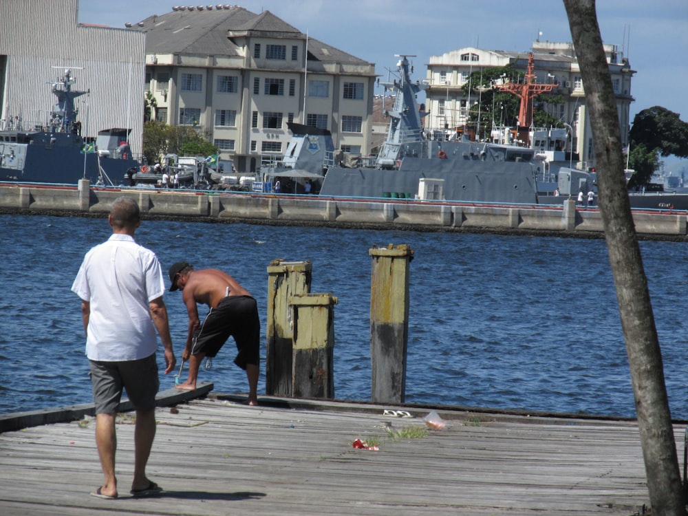 two men standing on a dock next to a body of water