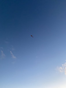 Colorful kite soaring high against a bright blue sky with wispy clouds