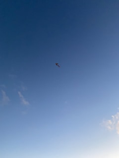 Colorful kite soaring high against a bright blue sky with wispy clouds