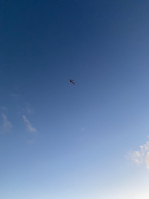 Colorful kite soaring high against a clear blue sky with wispy clouds.