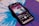 A smartphone displays a music player interface showing album art and song details on its screen. The phone is placed on a vibrant blue and purple vinyl record, which has a kaleidoscope-like pattern. The album cover features a psychedelic landscape with a celestial theme.