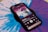 A smartphone displays a music player interface showing album art and song details on its screen. The phone is placed on a vibrant blue and purple vinyl record, which has a kaleidoscope-like pattern. The album cover features a psychedelic landscape with a celestial theme.
