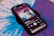A smartphone displays a music player interface showing album art and song details on its screen. The phone is placed on a vibrant blue and purple vinyl record, which has a kaleidoscope-like pattern. The album cover features a psychedelic landscape with a celestial theme.