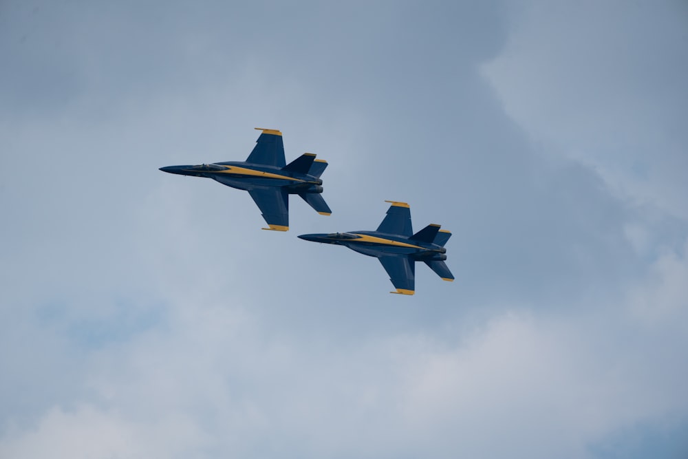 two blue fighter jets flying through a cloudy sky