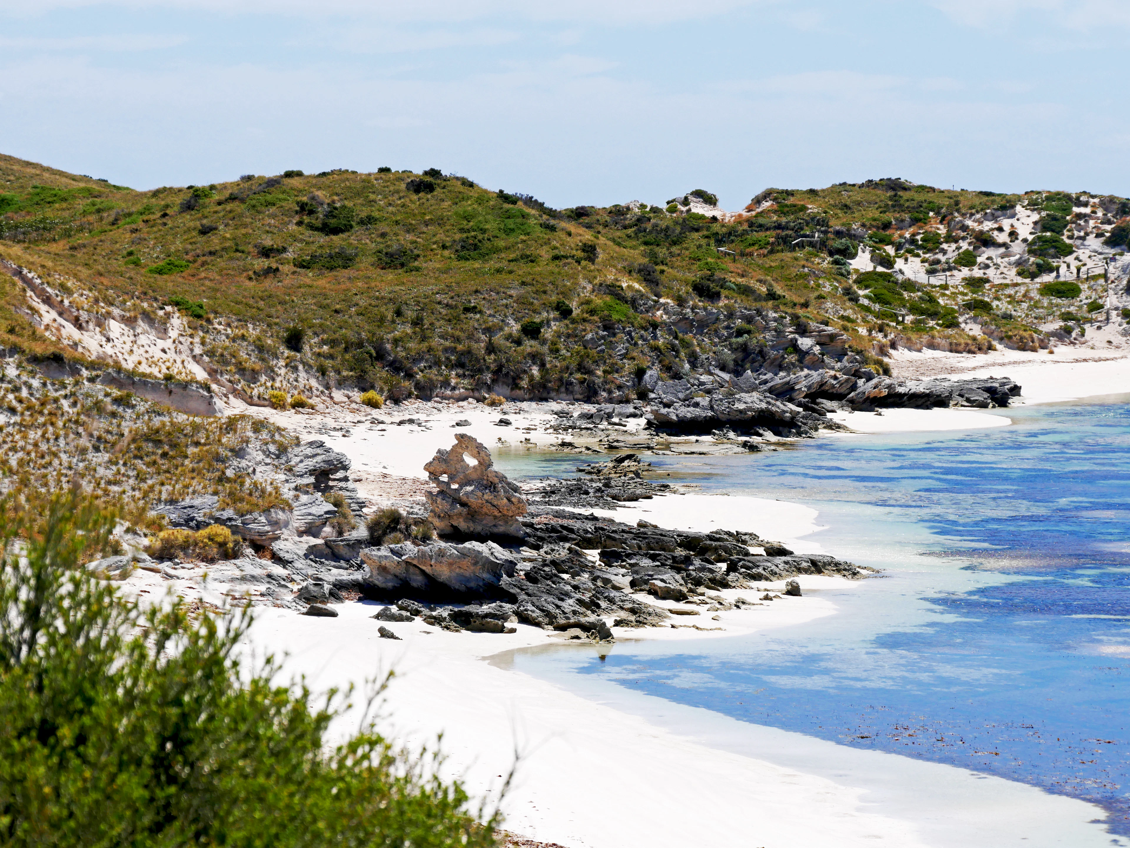 A white-sand cove and dark rocks beside clear water on Rottnest Island