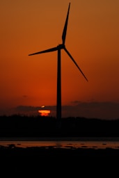the sun is setting behind a wind turbine