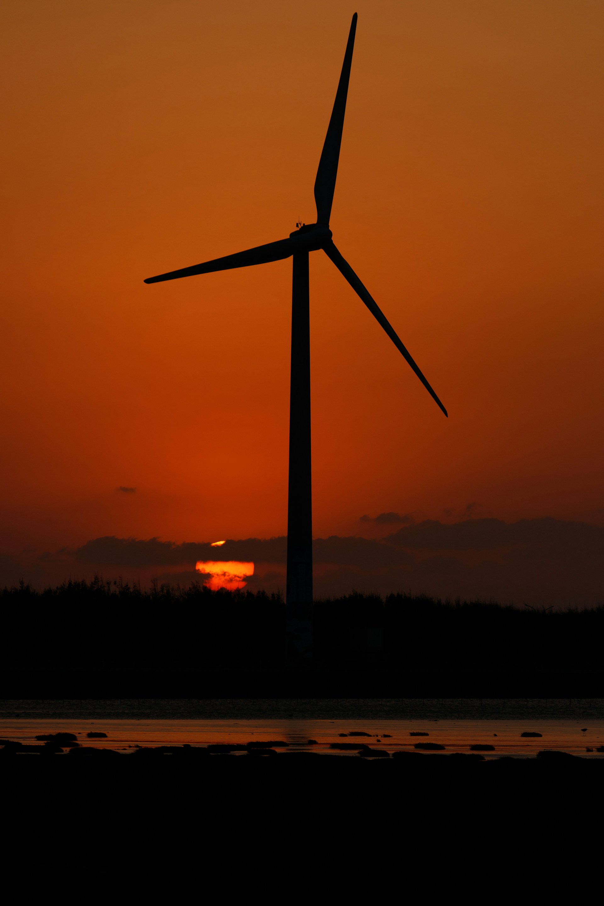 the sun is setting behind a wind turbine