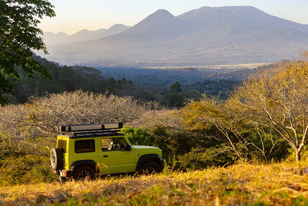 a yellow truck parked in a field with mountains in the background