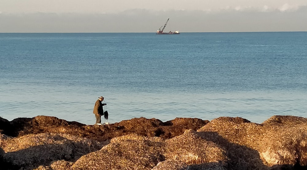 a man standing on top of a rocky beach next to the ocean