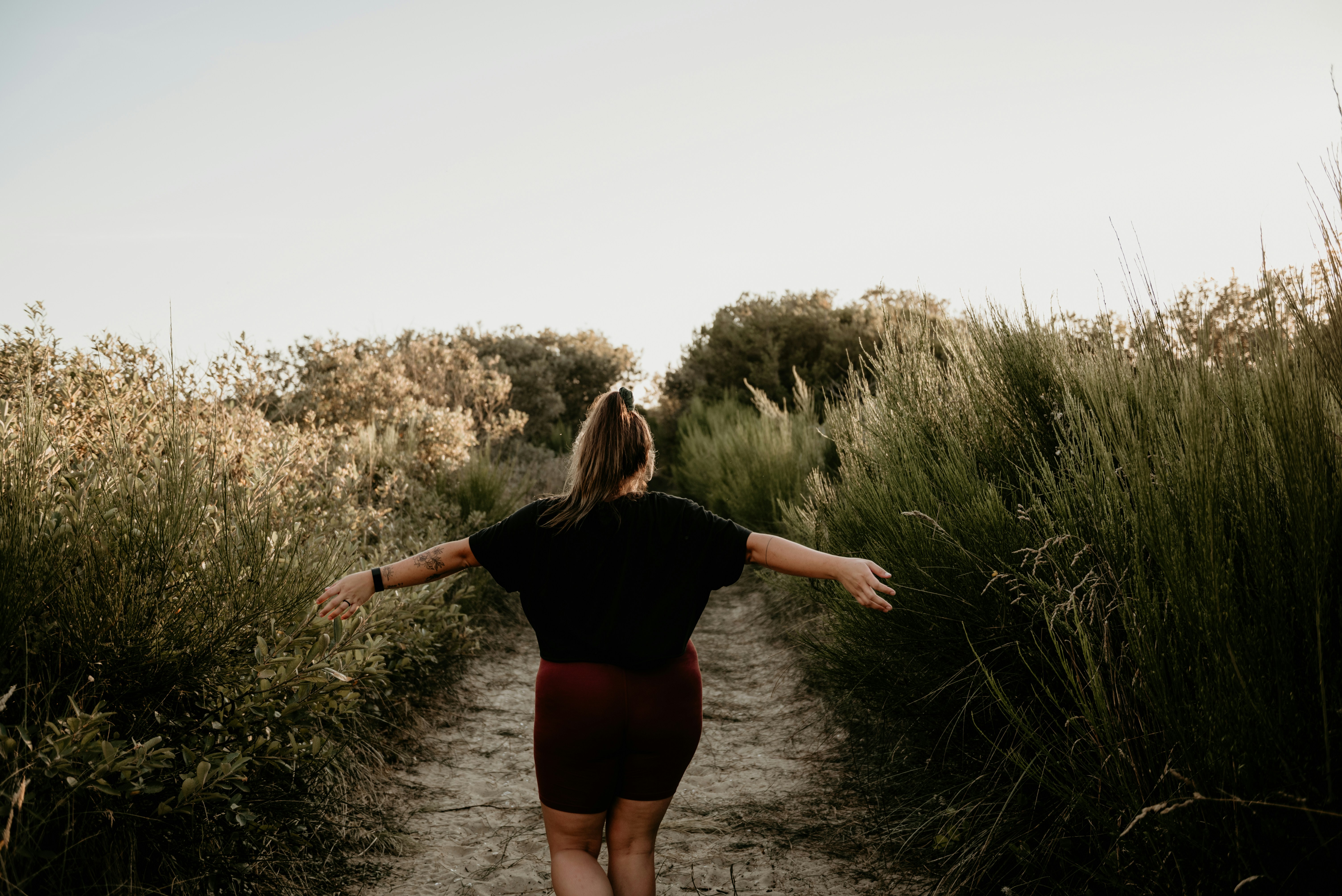 a woman walking down a dirt road with her arms outstretched