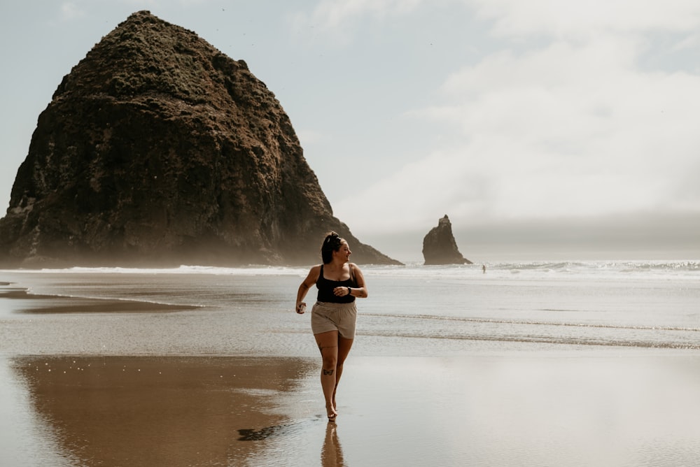 a woman walking along a beach next to a large rock