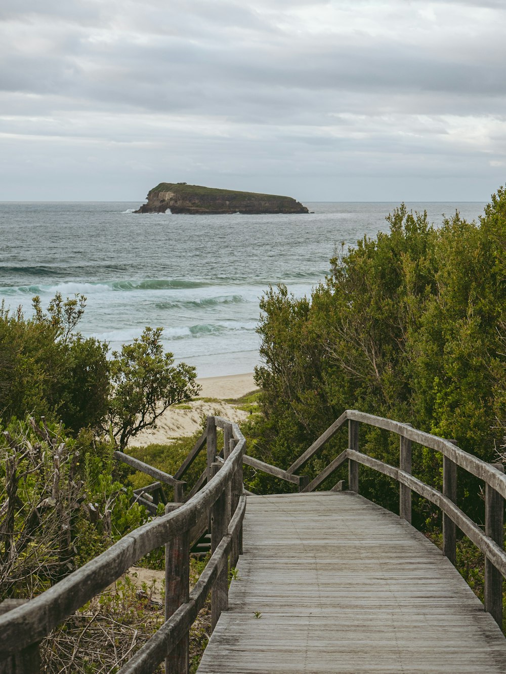 a wooden walkway leading to a beach with a small island in the distance