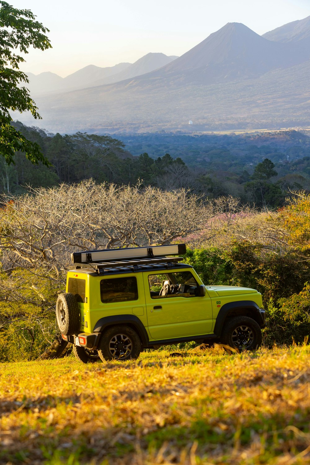 a yellow jeep parked in a field with mountains in the background
