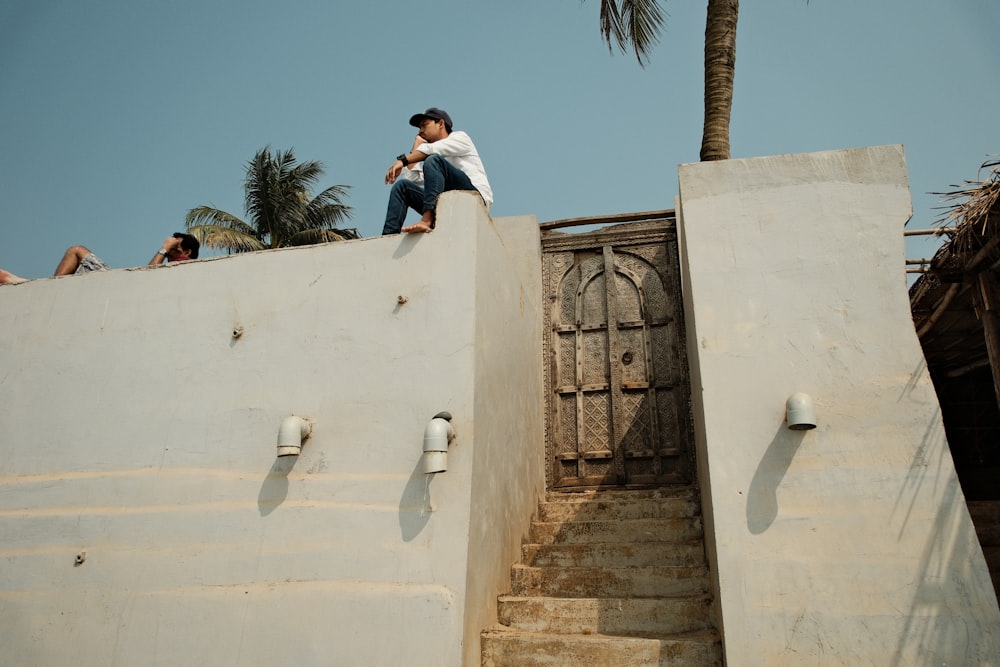 a man sitting on top of a cement wall next to a palm tree