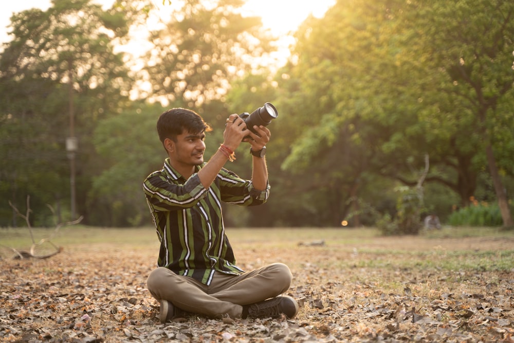 a young man sitting on the ground holding a camera