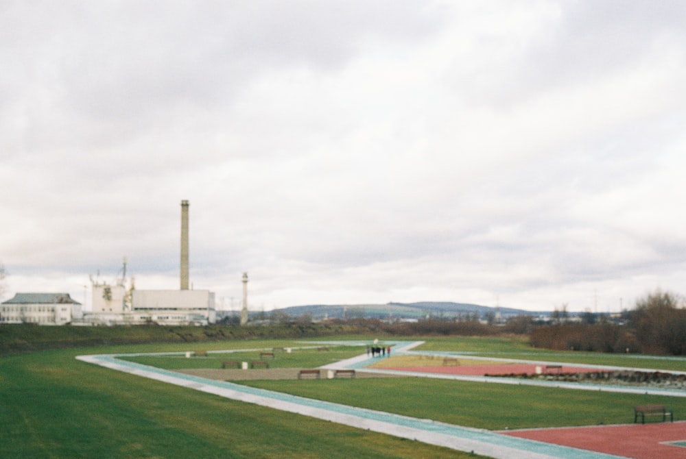 a large grassy field with a factory in the background