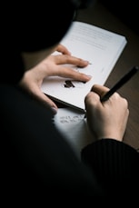 a person writing on a piece of paper with a pen