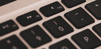 A close-up view of a laptop keyboard showing keys like F10, 0, and P arranged in a row. The keys are black with white symbols, and the surrounding area is silver.
