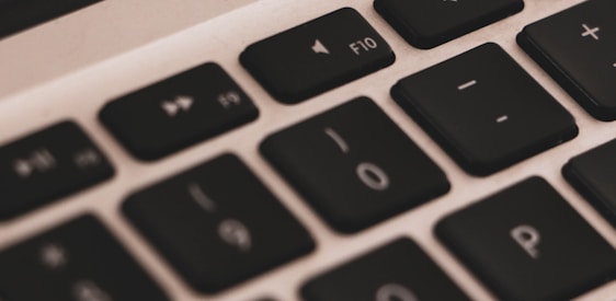A close-up view of a laptop keyboard showing keys like F10, 0, and P arranged in a row. The keys are black with white symbols, and the surrounding area is silver.