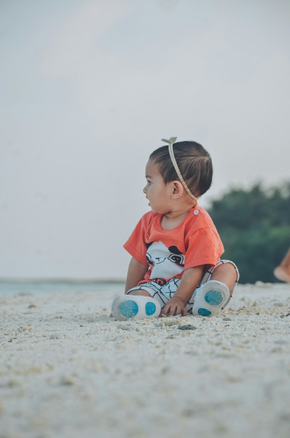 ein kleines Mädchen, das mit den Füßen im Sand am Strand sitzt