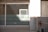 A glass window with horizontal frosted stripes and a light source casting a bright rectangle of light onto it. Surrounding the window is a white wall with some shadows. To the right, there's a concrete wall with a hose reel attached.