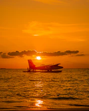 A sleek seaplane landing on turquoise Maldives waters at sunset.