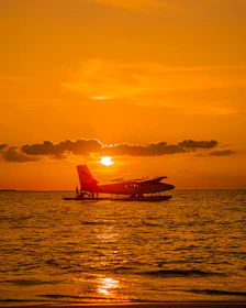 A sleek seaplane landing on turquoise Maldives waters at sunset.