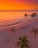 A serene beach scene at sunset with a vibrant orange and pink sky. Two overwater bungalows are visible in the background. On the sandy shore, there is a romantic setup with a heart shape outlined in red lights and a couple seated inside. The phrase 'WILL YOU MARRY ME?' is written in the sand.