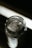 A glass jar filled with large, clear, crystalline structures, likely resembling rock salt or sugar crystals, placed against a dimly lit background which creates a strong contrast. The focus is on the top of the jar, highlighting the texture and form of the crystals inside.