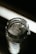 A glass jar filled with large, clear, crystalline structures, likely resembling rock salt or sugar crystals, placed against a dimly lit background which creates a strong contrast. The focus is on the top of the jar, highlighting the texture and form of the crystals inside.